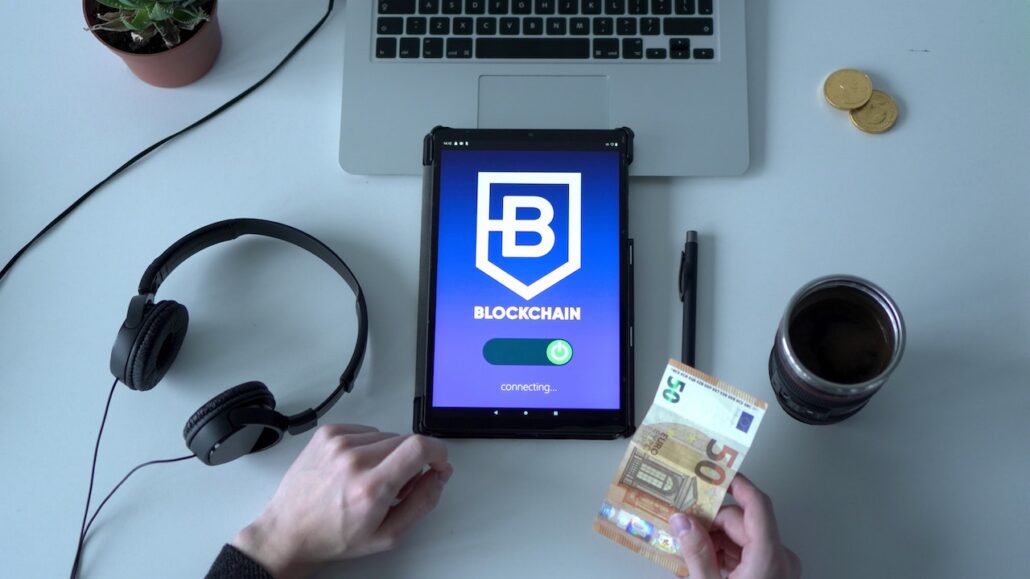 Stock photo of device with blockchain on it - cash in hand and other things on desk.